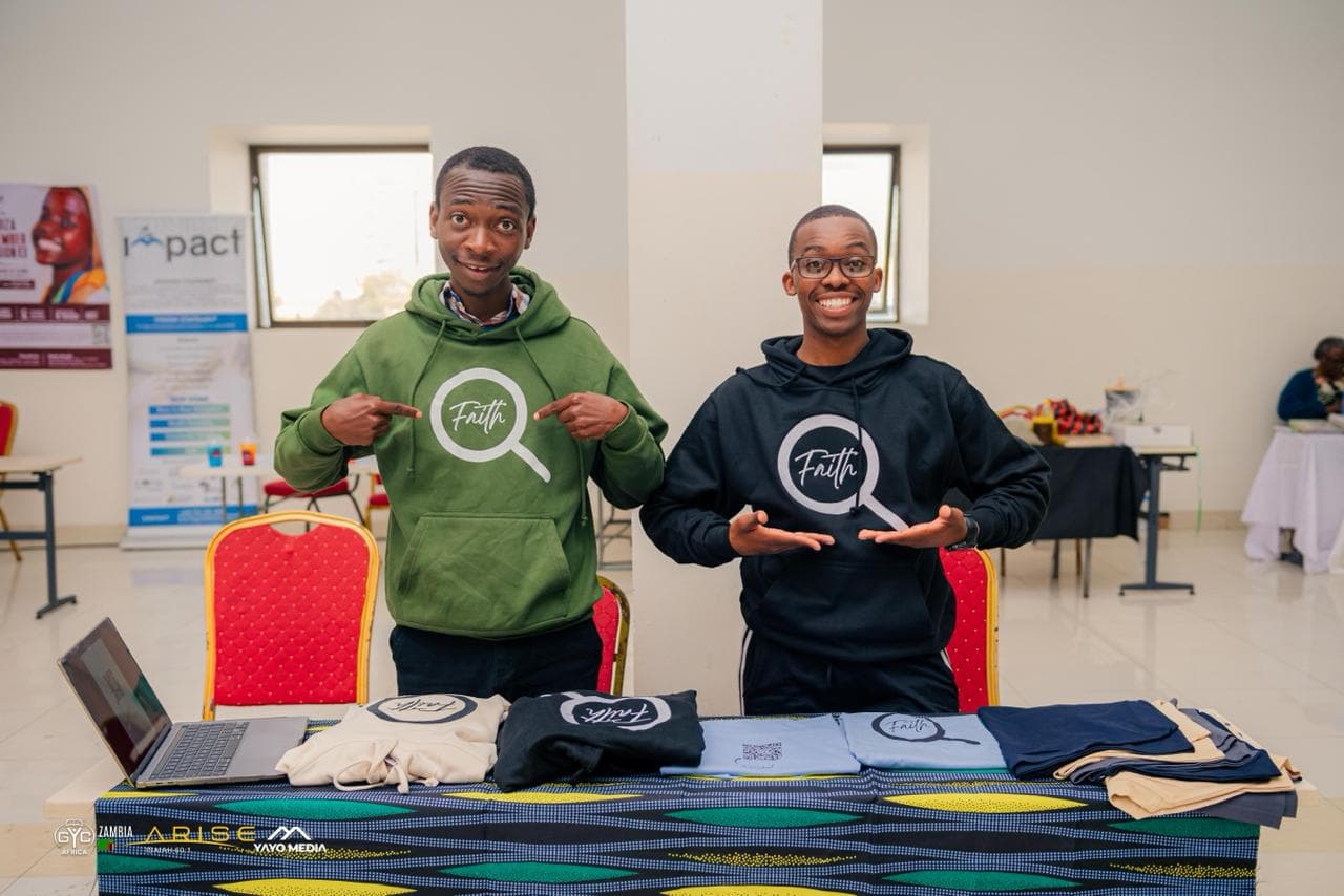 Two people in Faith hoodies smiling behind the FaithExplored stand at GYC Africa 2026