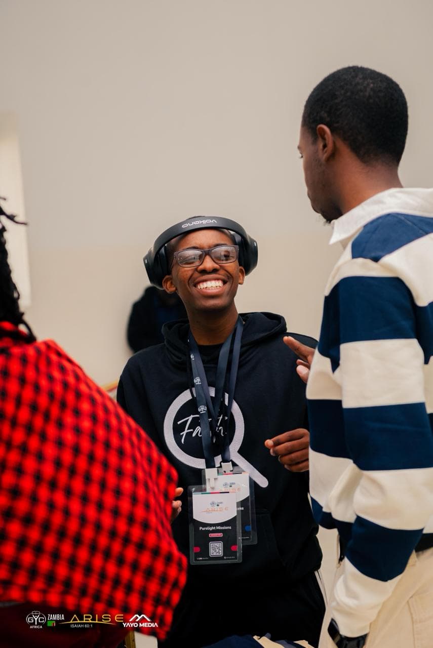 A smiling attendee in a black Faith hoodie chatting with another attendee